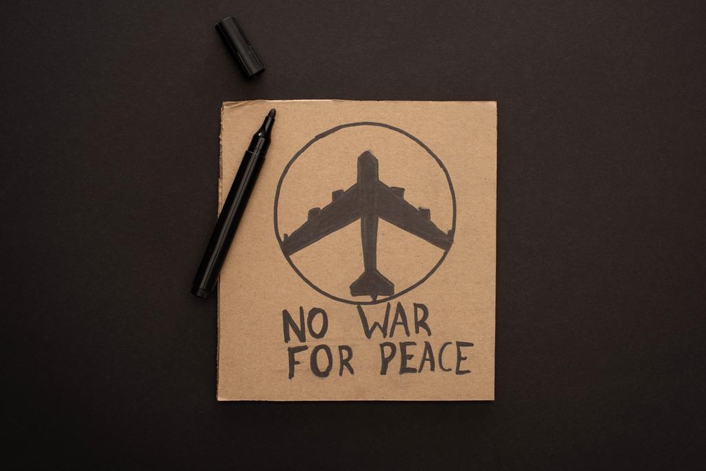 πάνω όψη χαρτονένιας πινακίδας χωρίς πόλεμο για γράμματα ειρήνης και αεροπλάνο κοντά σε μαρκαδόρο σε μαύρο φόντο - Φωτογραφία, εικόνα