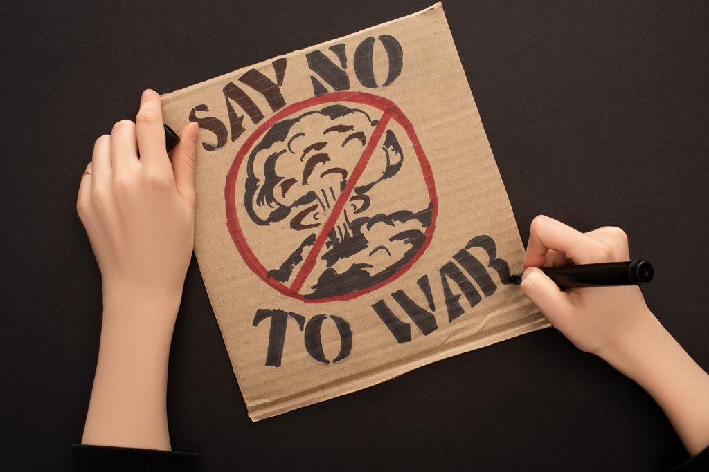 bijgesneden beeld van vrouw tekening bordje met zeggen nee tegen oorlog belettering op zwarte achtergrond - Foto, afbeelding