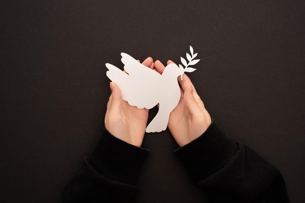 részleges kilátás a nő gazdaság fehér papír vágott galamb fekete háttér - Fotó, kép