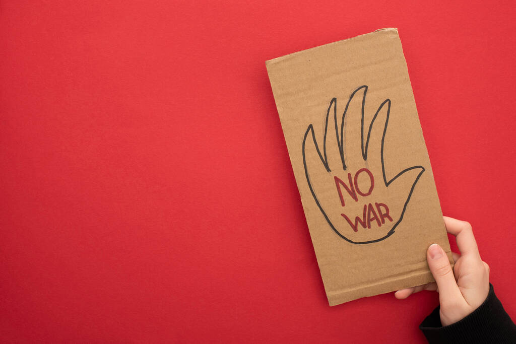κορυφαία άποψη της γυναίκας κρατώντας χαρτονένιο πλακάτ χωρίς γράμματα πολέμου σε κόκκινο φόντο - Φωτογραφία, εικόνα