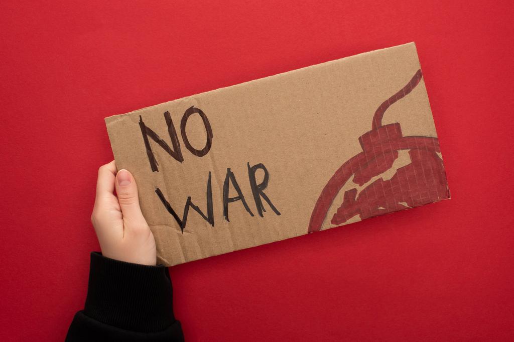 vista cortada de mulher segurando cartaz de papelão sem letras de guerra e bomba no fundo vermelho
 - Foto, Imagem