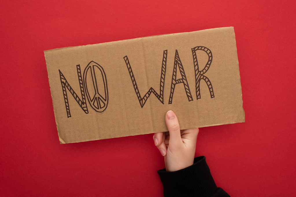обрезанный вид женщины с картонным плакатом без военных надписей на красном фоне
 - Фото, изображение