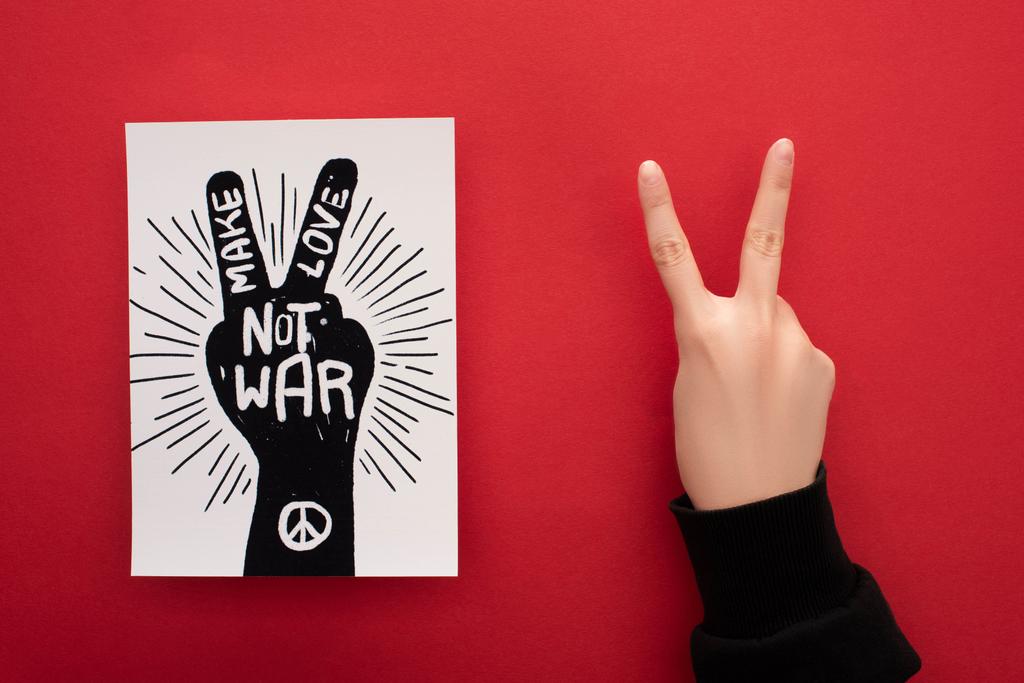 cropped view of woman showing peace sign near drawing with make love not war lettering and peace sign on red background - Photo, Image