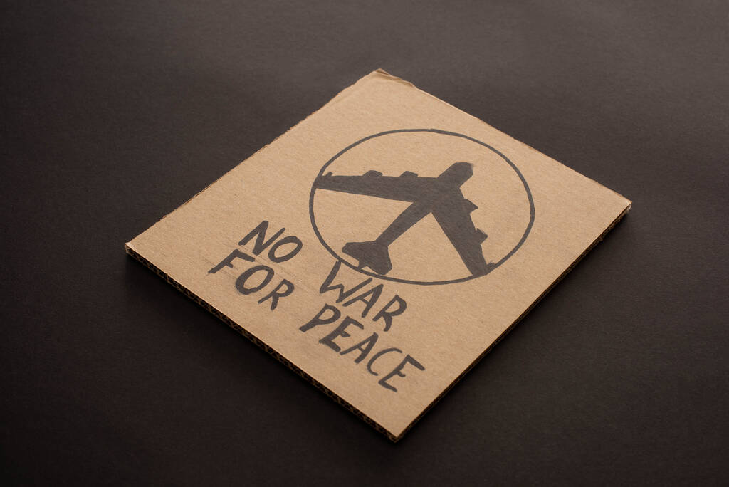 kartonnen bordje zonder oorlog om vredesbelettering en vliegtuig op zwarte achtergrond - Foto, afbeelding