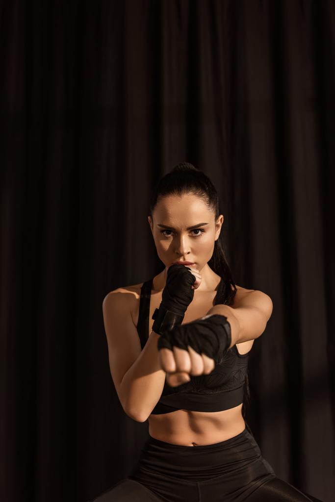 Atractiva deportista en posición de lucha con la mano extendida mirando a la cámara en negro
 - Foto, imagen