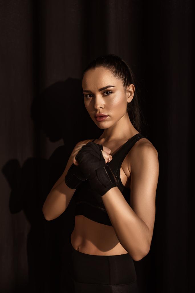 Aantrekkelijke sportvrouw in vechtpositie kijkend naar camera op zwart - Foto, afbeelding