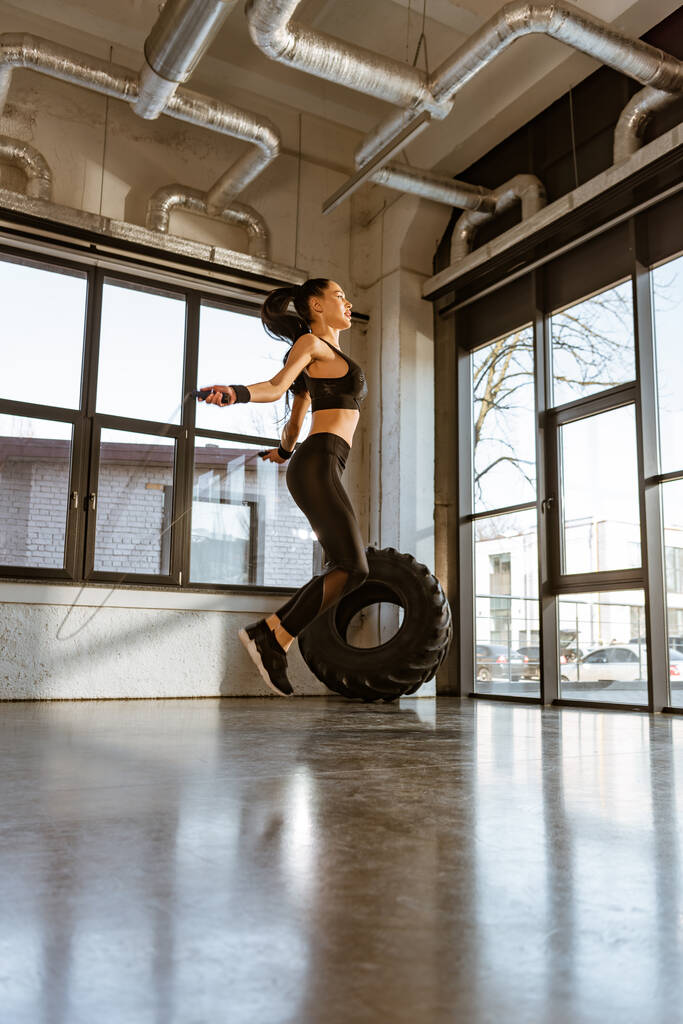 Widok z boku Sportswoman skoki z skakanką w siłowni - Zdjęcie, obraz