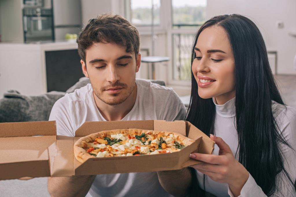 hermosa feliz pareja oliendo pizza caliente durante el auto aislamiento en casa
  - Foto, imagen