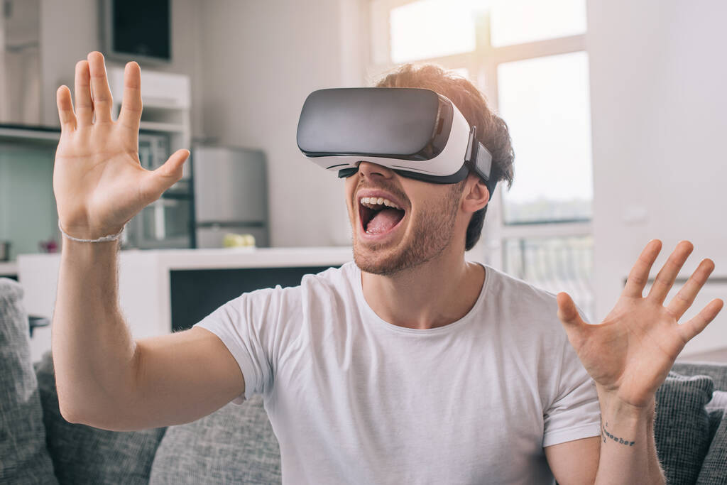возбужденный человек с помощью гарнитуры виртуальной реальности дома на самоизоляции
 - Фото, изображение
