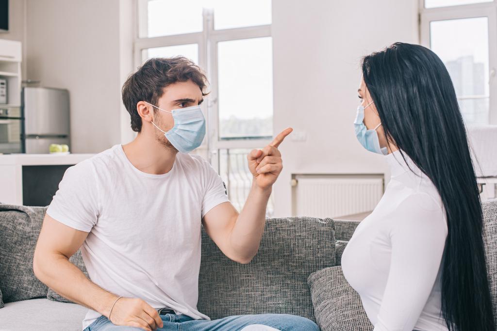 молода пара в медичних масках сваряться вдома під час самоізоляції
 - Фото, зображення