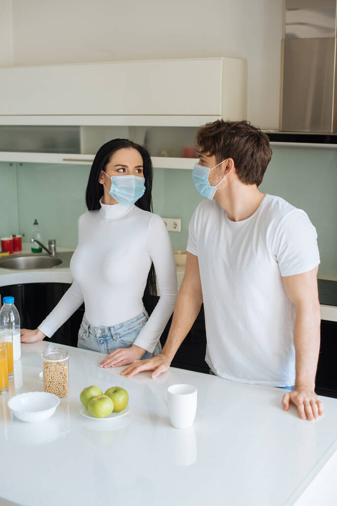 自立中に家で朝食をとる医療用マスクの美しいカップル - 写真・画像