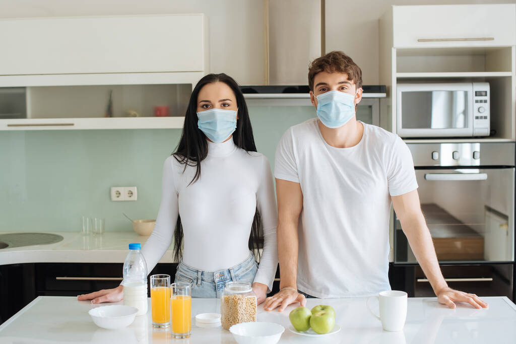 couple in medical masks having breakfast at home during self isolation - Photo, Image