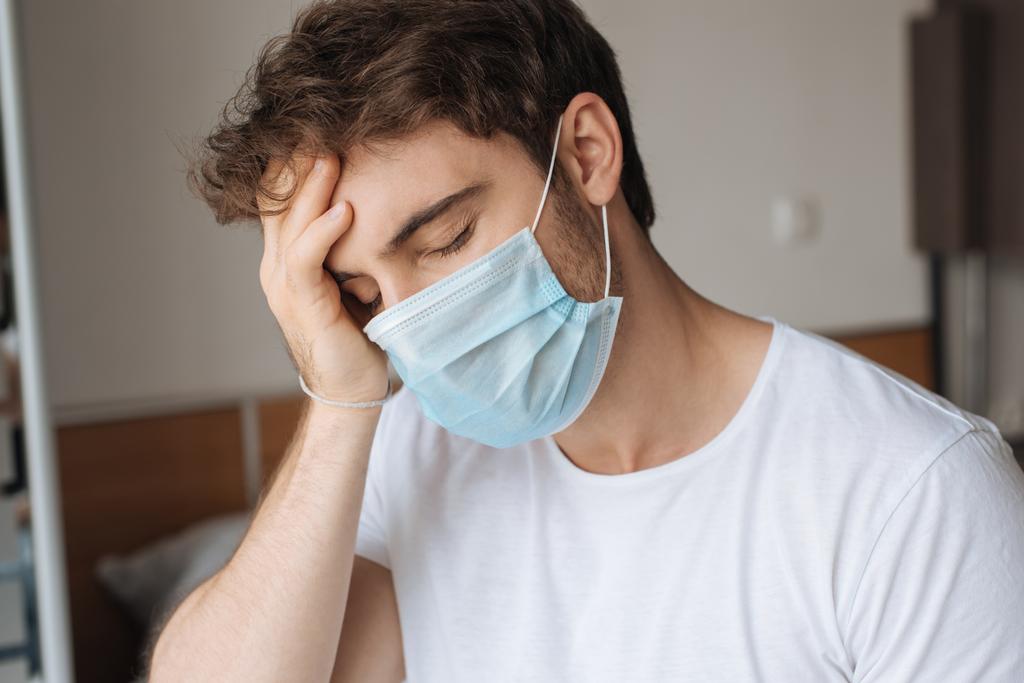 измученный больной человек в медицинской маске сидит в спальне во время самоизоляции
 - Фото, изображение
