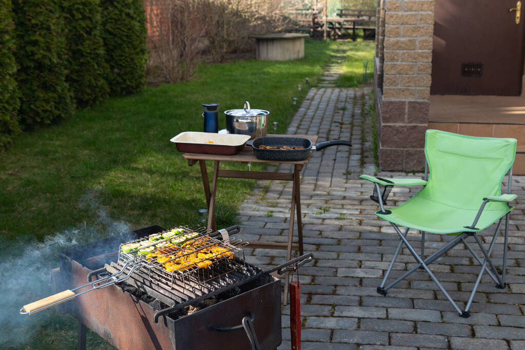 barbecue grillezett zöldségekkel, füsttel. összecsukható szék és egy kis asztal. A ház tornáca és a hátsó udvar a háttérben. Tavasz. nyár - Fotó, kép