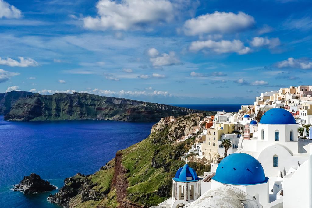 Santorini 'de beyaz evler ve deniz kenarındaki mavi kubbeli kiliseler.  - Fotoğraf, Görsel