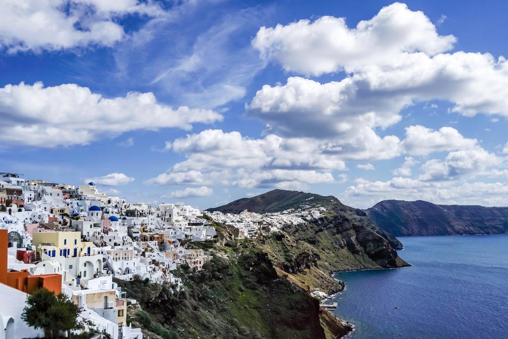 witte huizen in de buurt van rustige zee tegen blauwe lucht met wolken in Griekenland  - Foto, afbeelding