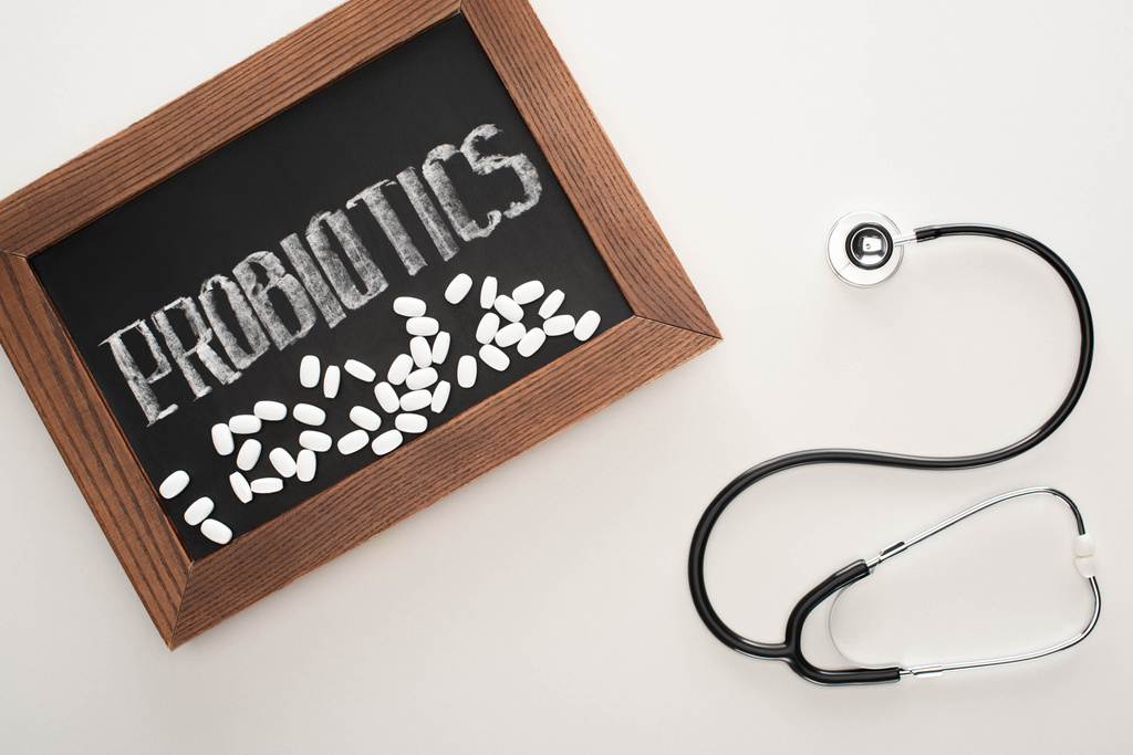 bovenaanzicht van krijtbord met probiotica belettering met pillen en stethoscoop op witte achtergrond - Foto, afbeelding