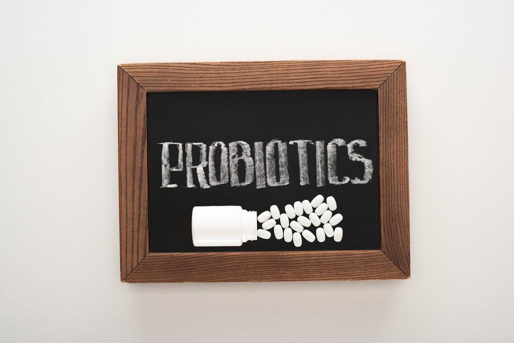 Kreidetafel mit Probiotika-Schriftzug mit Pillen und Behälter auf weißem Hintergrund - Foto, Bild