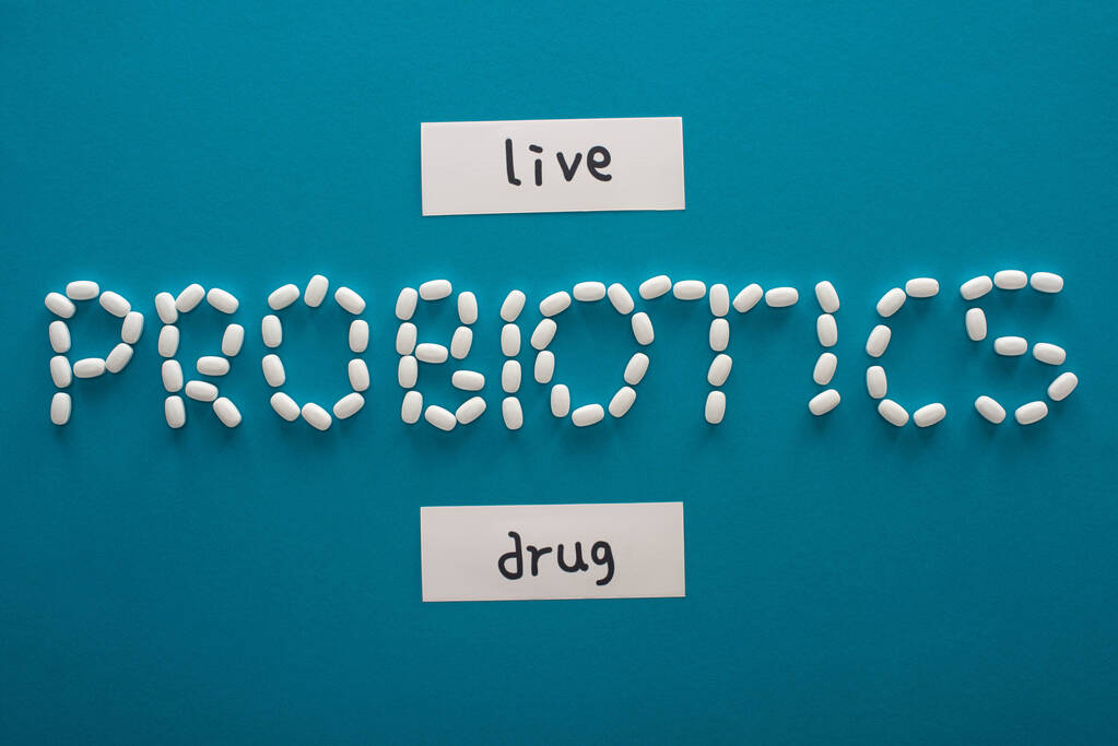 top view of probiotics lettering made of pills near paper cards with live and drug words on blue background - Photo, Image