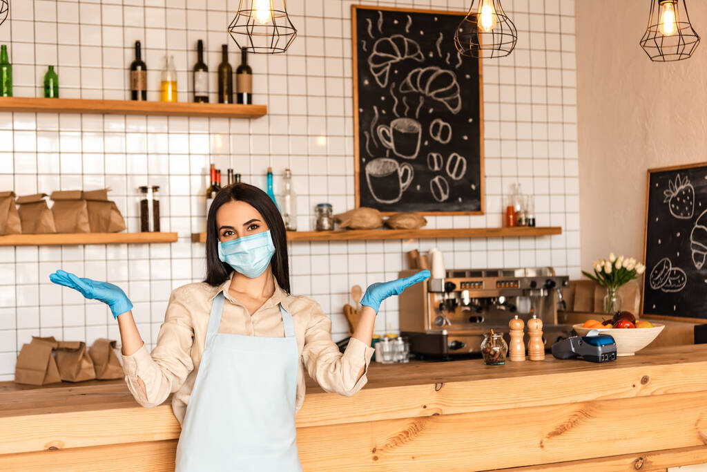 Propriétaire d'un café à bras ouverts avec masque médical et gants en latex regardant la caméra près de la table
 - Photo, image