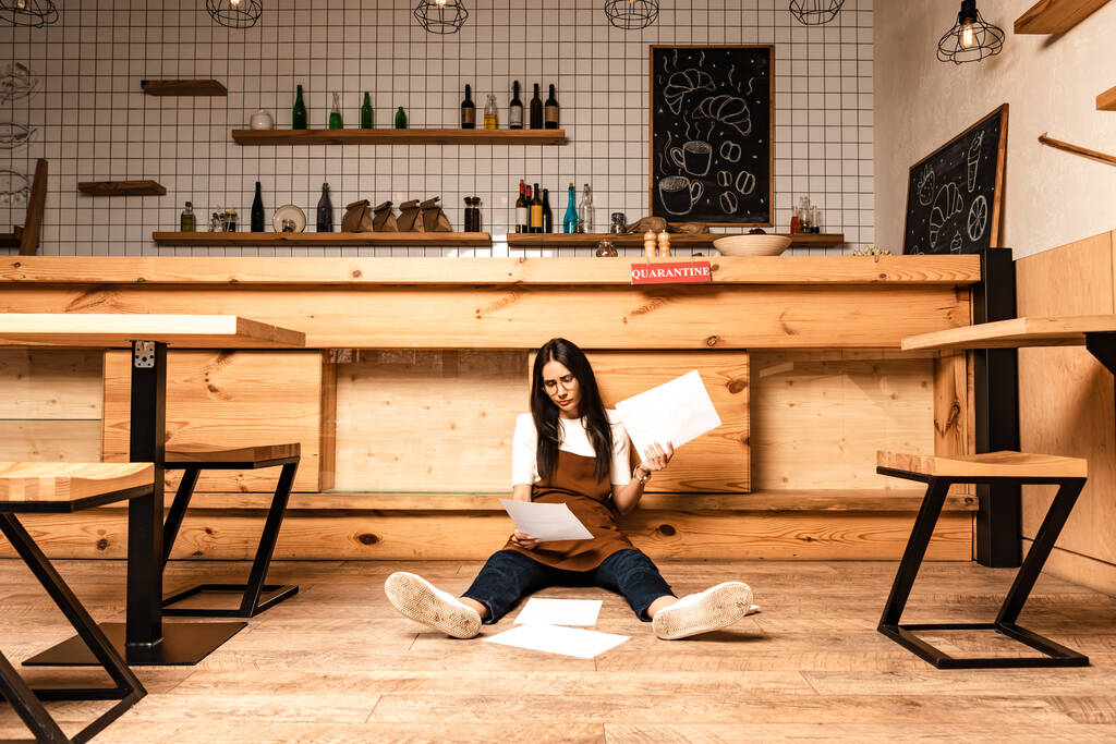 Skoncentrowany właściciel kawiarni patrząc na dokument i siedząc przy stole na podłodze - Zdjęcie, obraz