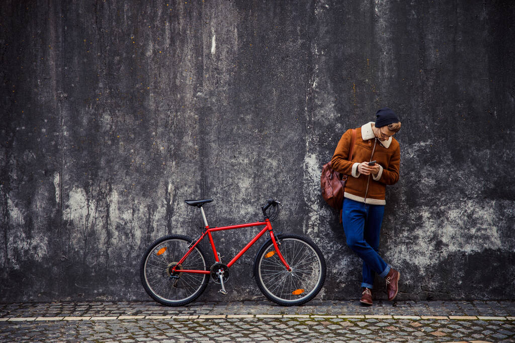 Спокійний чоловік з мотоциклом і смартфоном дивиться вниз стокове фото
 - Фото, зображення