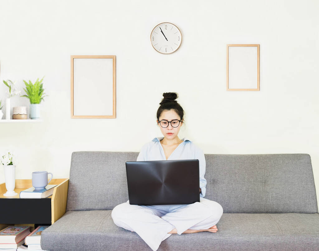 Молодая красивая азиатская женщина носила синюю рубашку, сидя на сером диване, работа онлайн образ жизни, расслабиться дома с кофейной кружкой, домашний рабочий ноутбук, работа из дома
 - Фото, изображение