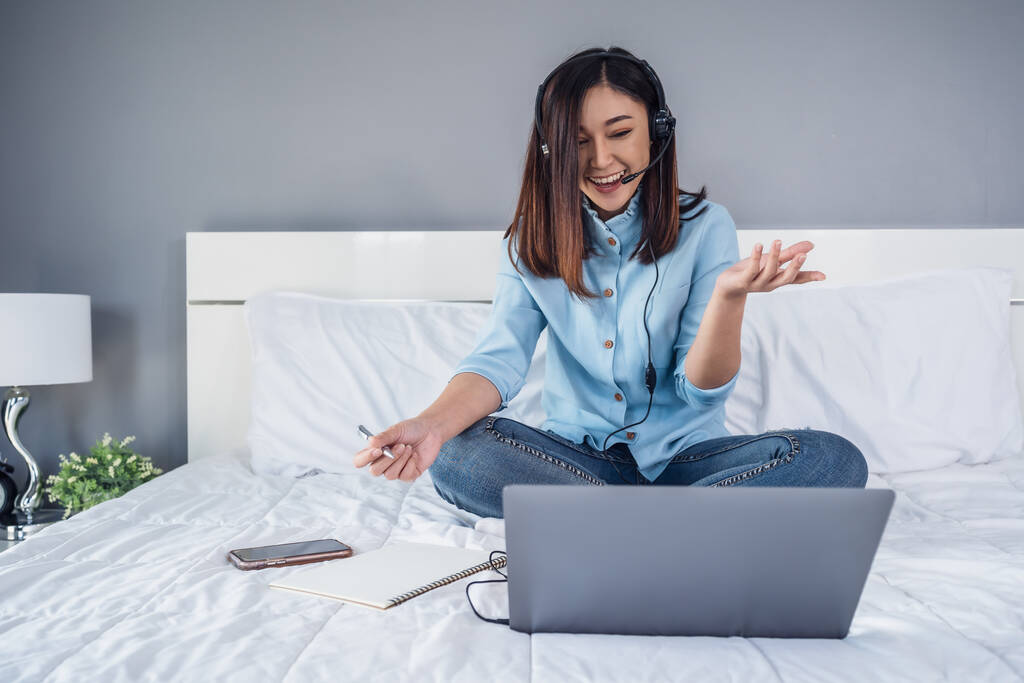 zakenvrouw dragen headset video conferentie bellen op laptop computer op een bed, werken vanuit huis concept - Foto, afbeelding