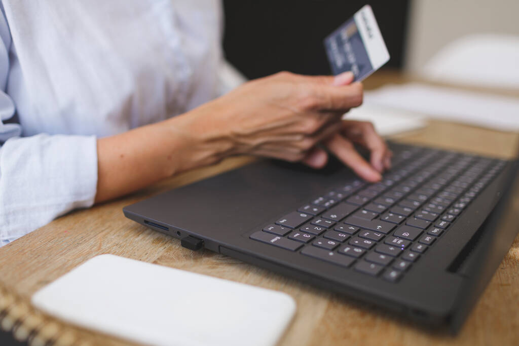 bijgesneden schot van het bedrijfsleven vrouw doet thuis winkelen met haar laptop en creditcard op de keukentafel - Foto, afbeelding