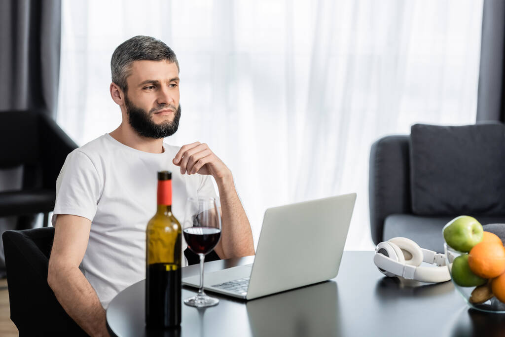 Вибірковий фокус працівника, який дивиться на ноутбук біля вина та фруктів на столі
 - Фото, зображення