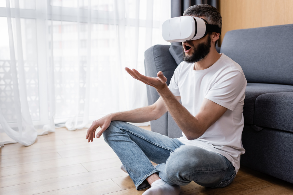 Geschockter Mann mit Kopfhörer sitzt auf dem Boden im Wohnzimmer - Foto, Bild