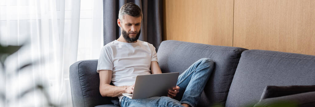 Orientação panorâmica de belo teletrabalhador usando laptop na sala de estar
 - Foto, Imagem