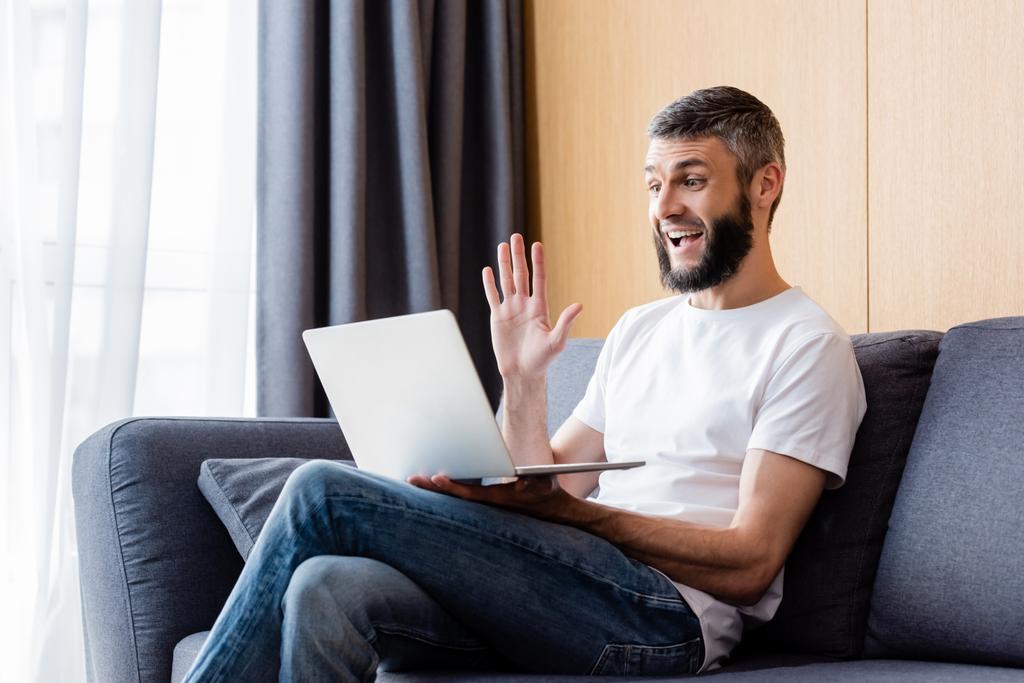 Vista lateral do teletrabalhador positivo ter vídeo chat no laptop na sala de estar
 - Foto, Imagem