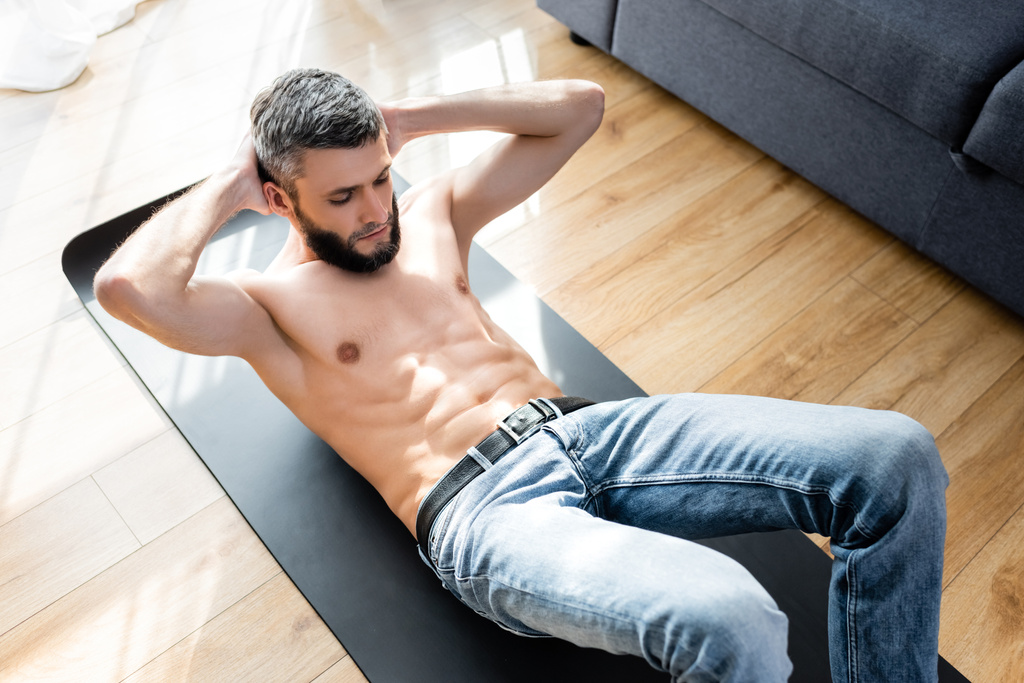 Wysoki kąt widzenia muskularny mężczyzna robi mięśnie brzucha podczas treningu na macie fitness w domu  - Zdjęcie, obraz