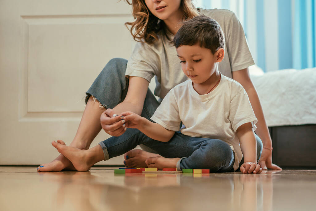 madre jugando con su hijo pequeño mientras está sentada cerca de juguetes en el suelo
  - Foto, imagen