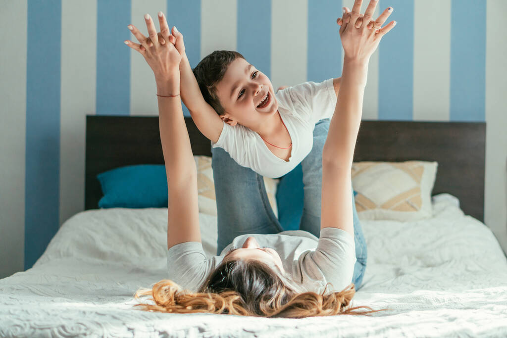 foco seletivo da mãe deitada na cama e de mãos dadas com o filho da criança enquanto brincava no quarto
  - Foto, Imagem