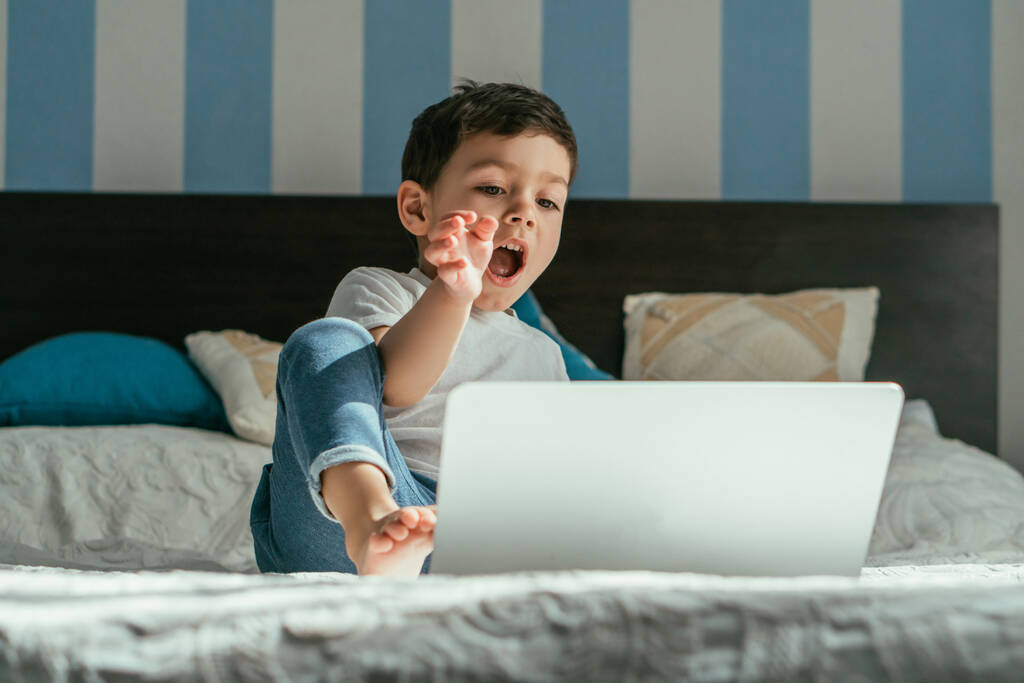 вибірковий фокус емоційного малюка хлопчика жестикулюючи, дивлячись на ноутбук в спальні
  - Фото, зображення