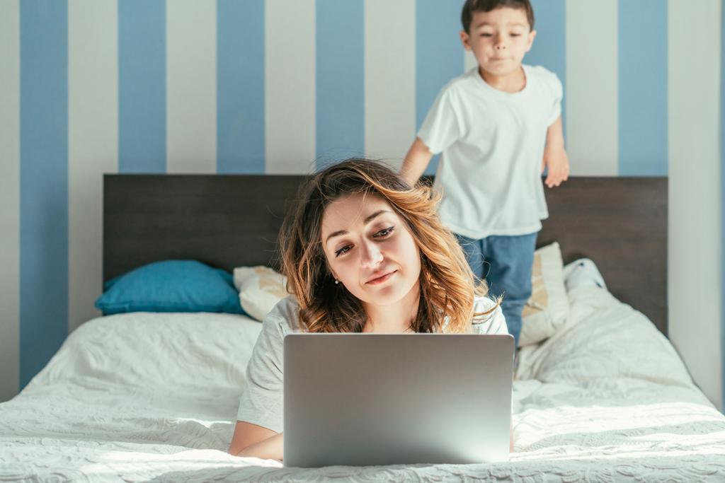 enfoque selectivo de freelancer que trabaja desde casa cerca de su hijo pequeño en el dormitorio
  - Foto, imagen
