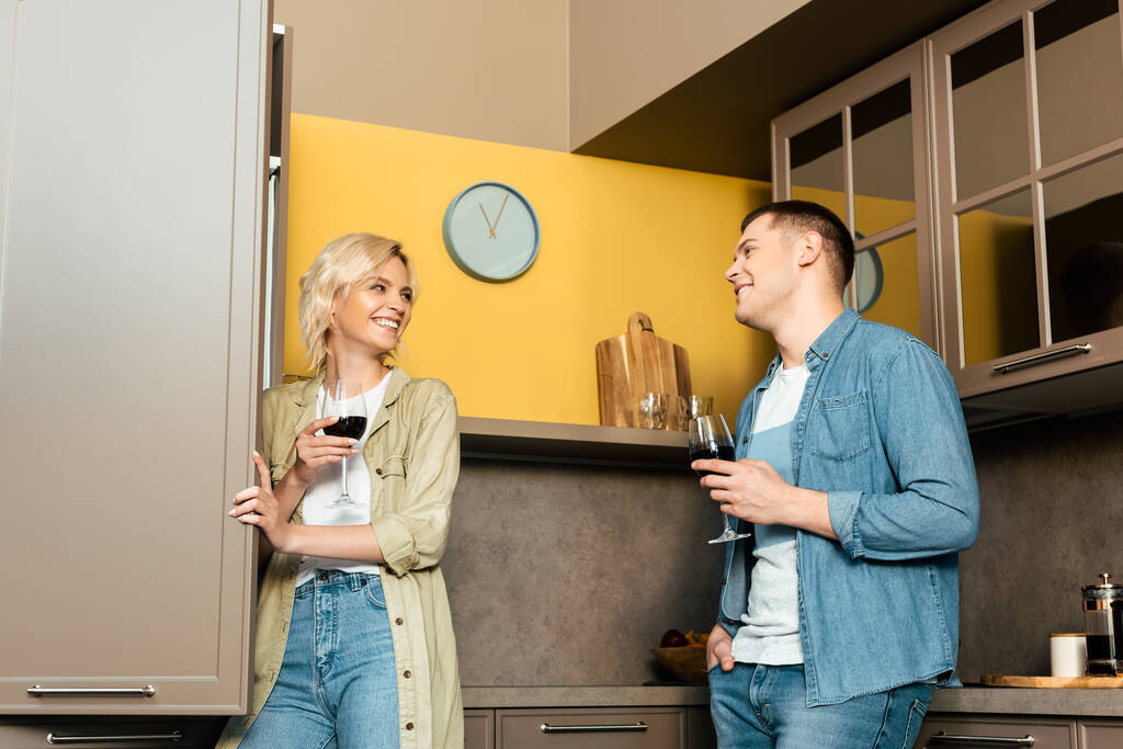 χαμογελαστό ζευγάρι πίνοντας κόκκινο κρασί μαζί στην κουζίνα - Φωτογραφία, εικόνα