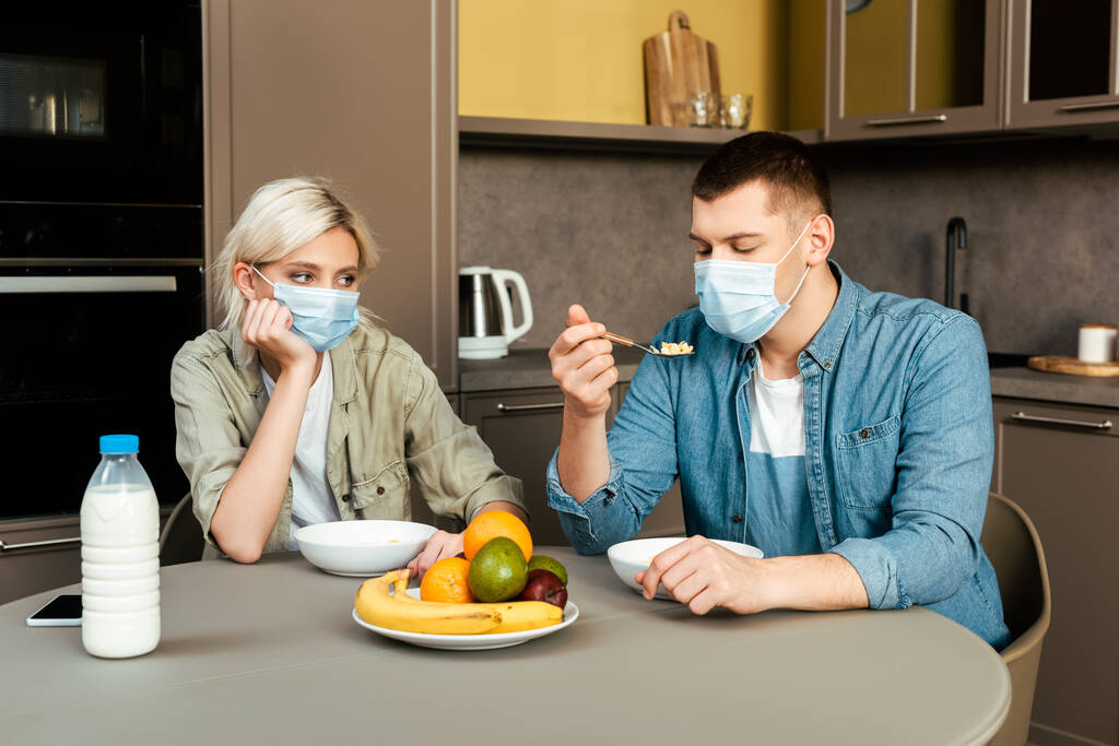pár orvosi maszkok eszik reggeli a konyhában - Fotó, kép