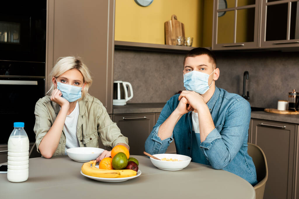 couple en masques médicaux prenant le petit déjeuner dans la cuisine
 - Photo, image