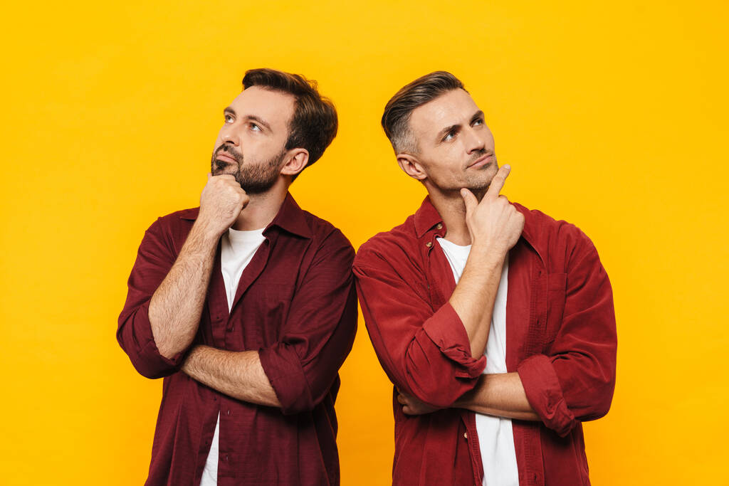 2人のハンサムな男性のイメージ30代の赤いシャツを考え、上を向いてコピースペースを見ます黄色の背景に孤立 - 写真・画像