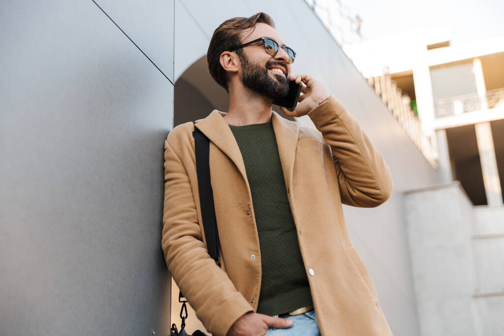 Obrázek pohledný kavkazský vousatý dospělý muž ve slunečních brýlích mluví na smartphone a stojí venku - Fotografie, Obrázek