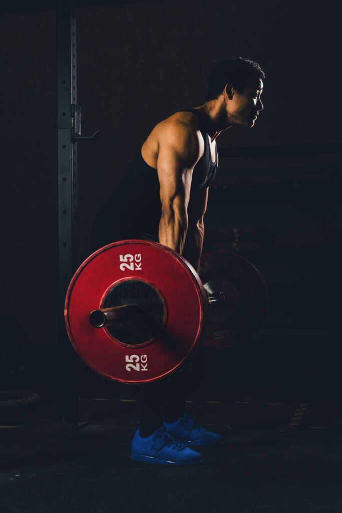 Азійський сильний чоловік, який займається фізичними вправами та будує корпус з барилами, важить у спортзалі та в центрі фітнесу в темному тоні. - Фото, зображення