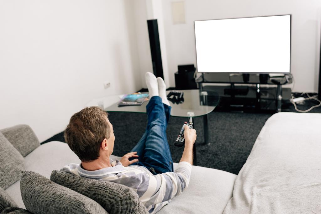 muž v džínách drží dálkový ovladač v blízkosti bílé televizní obrazovky doma  - Fotografie, Obrázek