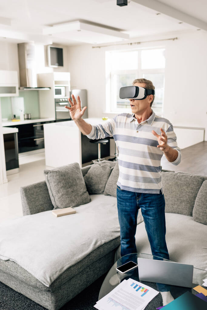 uomo sorpreso in realtà virtuale auricolare gesticolare a casa
  - Foto, immagini