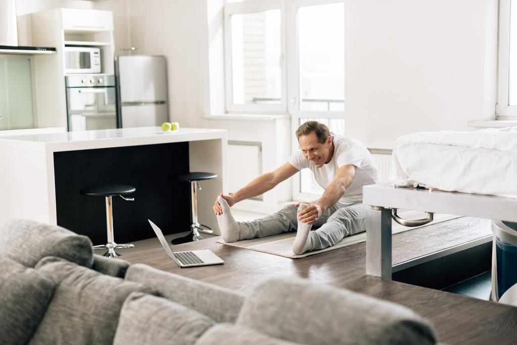 selektivní zaměření šťastný muž protahování a sledování online cvičení na notebooku doma  - Fotografie, Obrázek