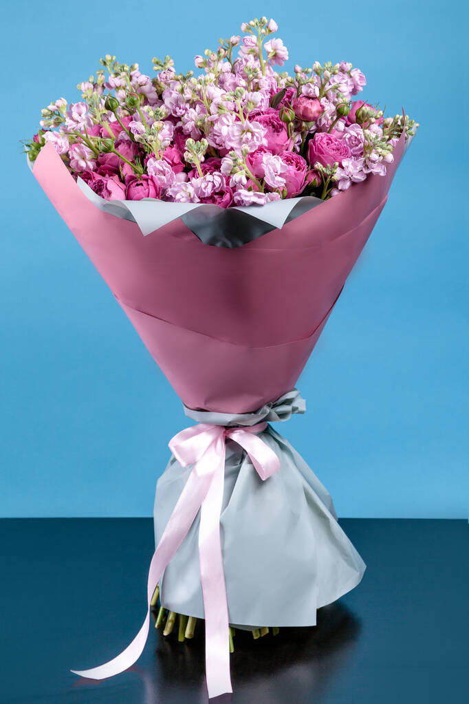 kukkakimpun ruusuja ja Mattioli vaaleanpunainen pakkaus sinisellä taustalla. korkea laatu
. - Valokuva, kuva