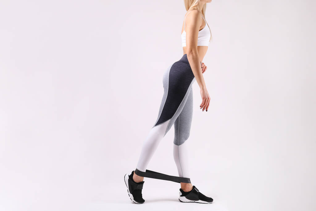Close-up shot van onherkenbare fit vrouw dragen van een lege tank top & yoga broek, doet oefeningen met fitness band. geïsoleerd op witte achtergrond. Aantrekkelijk vrouwtje in sportkleding. Kopieer ruimte voor tekst. - Foto, afbeelding