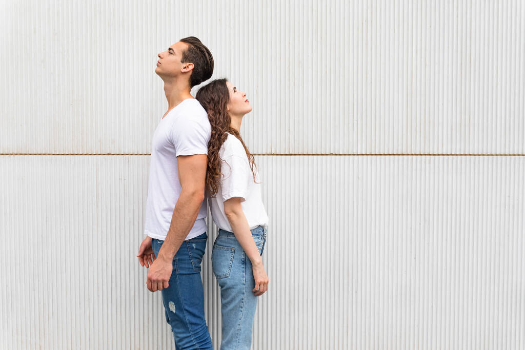 Junges fröhliches Paar steht Rücken an Rücken gegen weiße Stadtmauer - Foto, Bild
